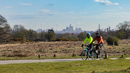 two people cycling in Richmond Park with the London skyline in the distant background.
