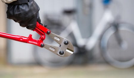 Bike thief with black gloves and red boltcutters stealing locked bicycle