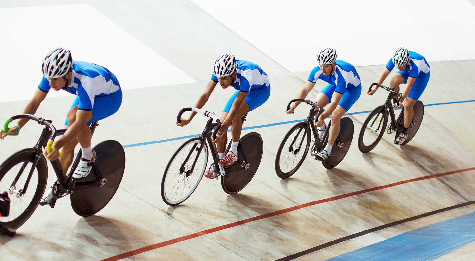 Group of cyclists in race competition riding in a line wearing blue vests in a velodrome